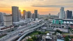 City skyline with high-rise buildings and busy highway during sunset under cloudy sky