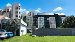 Modern residential blocks behind a construction site with sound barrier fencing under blue sky