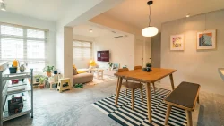 Open-plan dining and living room with wooden furniture, striped rug, wall art, plants and large windows with blinds