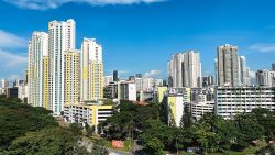 Cluster of tall residential blocks and housing blocks surrounded by green trees under a blue sky