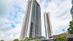 Two tall residential apartment blocks with balconies against a partly cloudy sky and greenery below