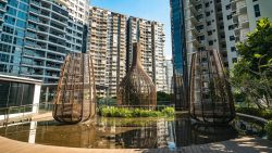 High-rise apartment blocks behind decorative metal sculptures reflected in water feature at residential complex courtyard
