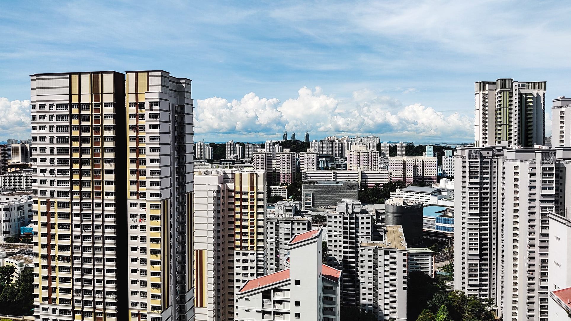 High-rise residential blocks with yellow and beige accents under a partly cloudy sky in an urban area
