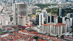 Dense cityscape with high-rise commercial buildings, red-roofed heritage shophouses and lush greenery in the background