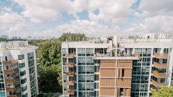 Floridian apartment blocks with rooftop terraces beside lush greenery under a partly cloudy sky