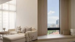Living room with cream sofa, cushions, ottoman and round wooden side table beside window with city view