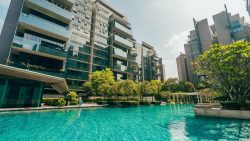 Residential apartment blocks with balconies beside a swimming pool and surrounding landscaped greenery