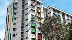 White HDB flat with colourful painted panels and laundry hanging outside windows on a sunny day