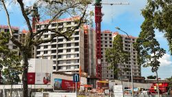 Unfinished residential blocks under construction with cranes and machinery, surrounded by trees and safety barriers