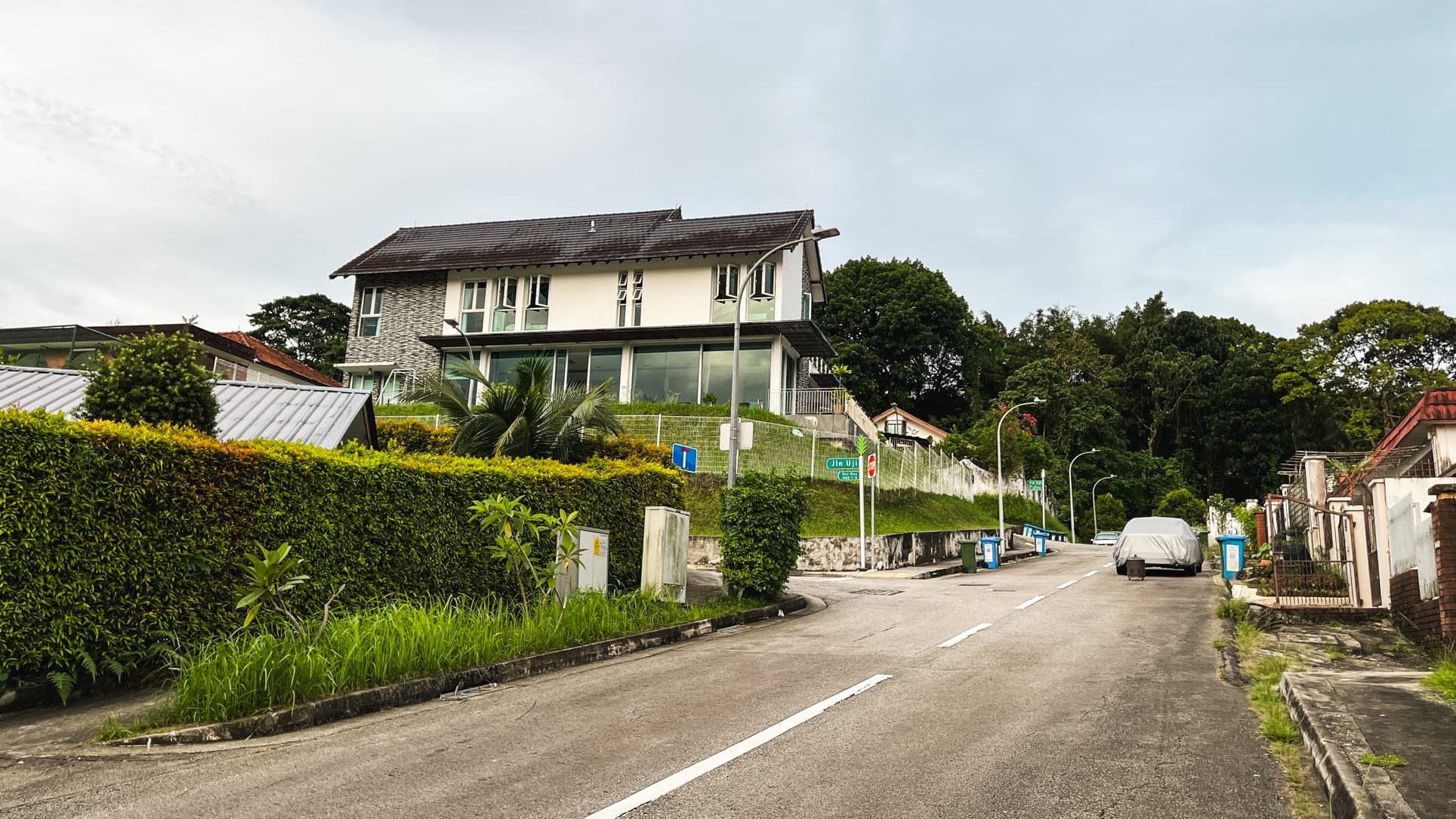Large two-storey residential house on a hill with greenery along a quiet street and covered car parked