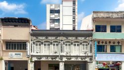 Two-storey conserved shophouses with intricate carvings flanked by simpler older shophouses and a modern apartment block behind