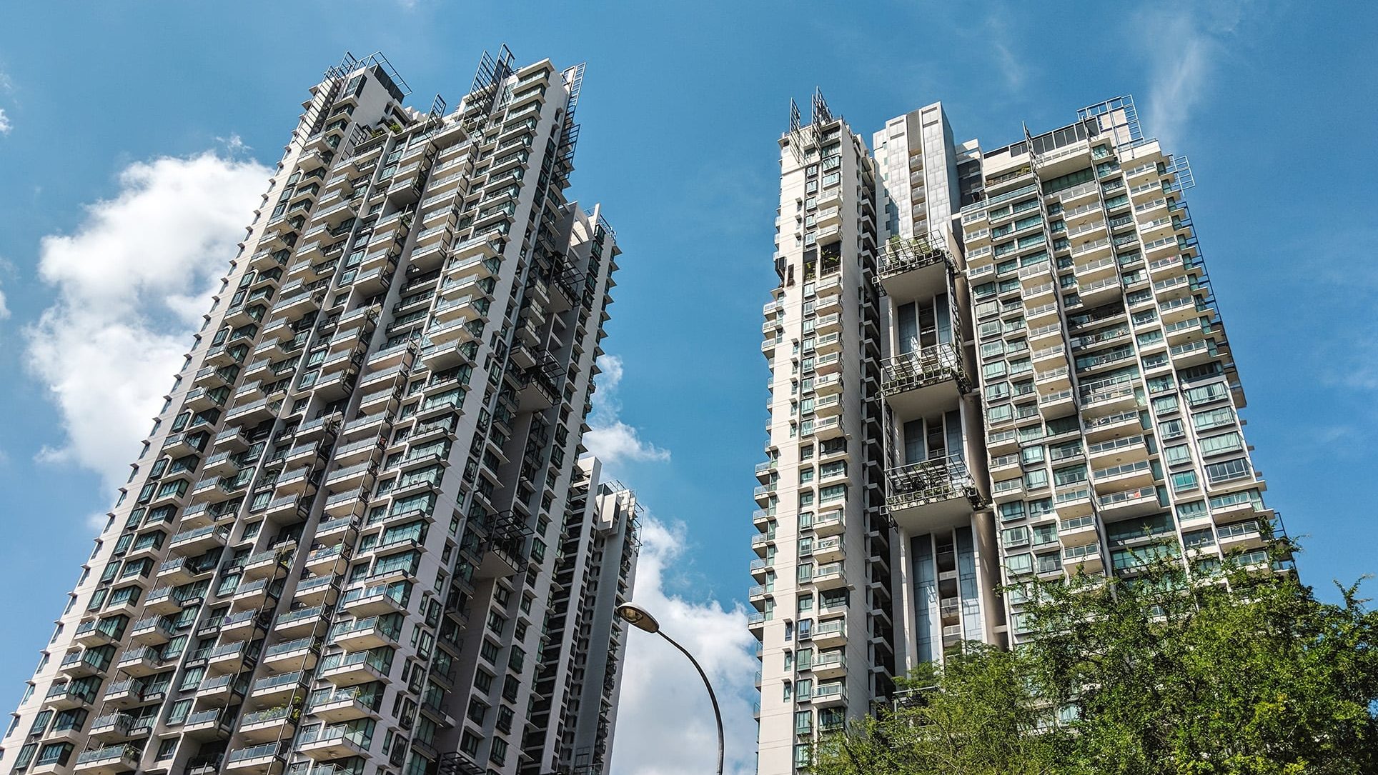 Two tall Rivergate apartment towers with balconies under a partly cloudy blue sky