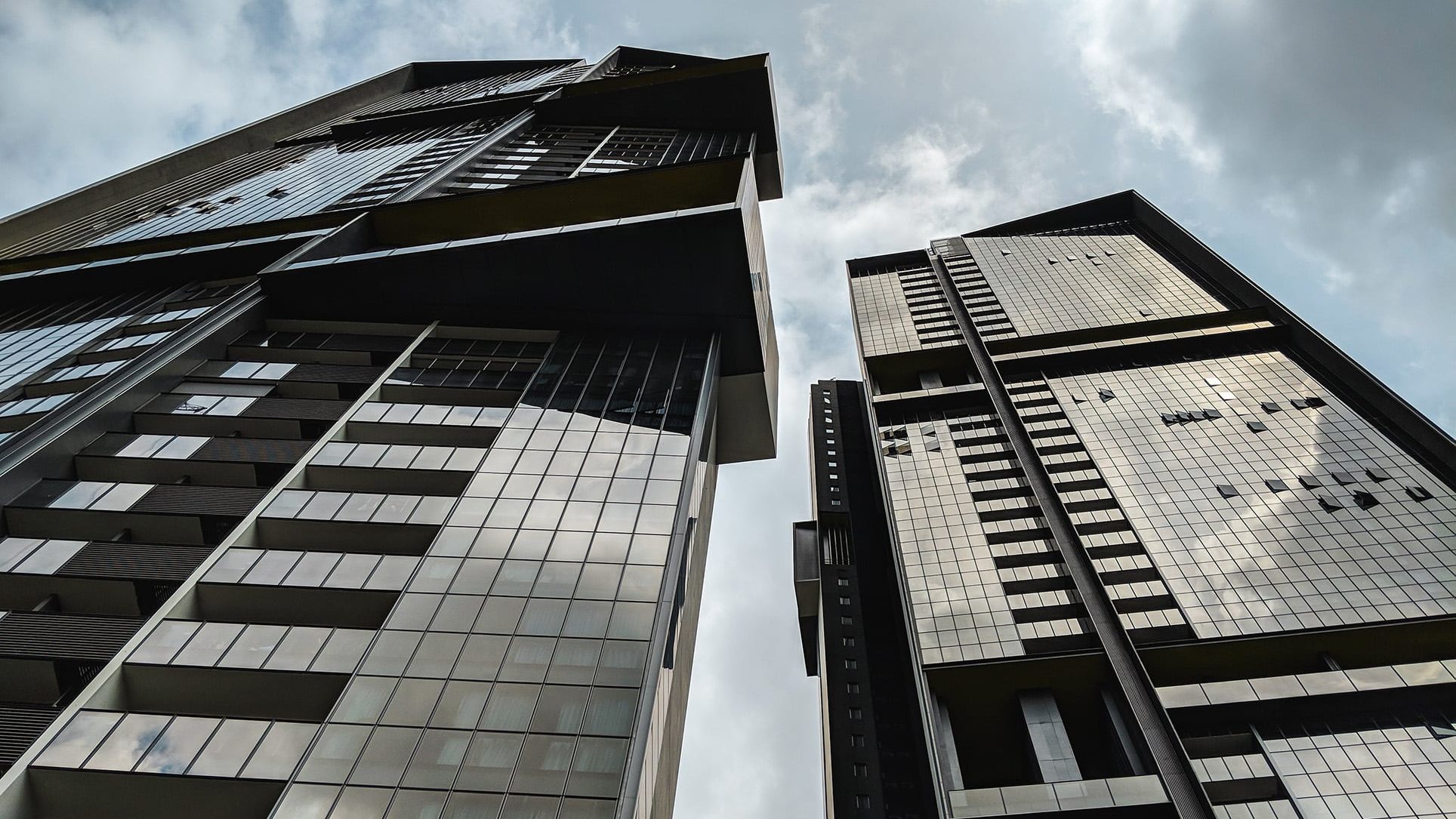 Echelon residential blocks with glass facades and balconies under a cloudy sky