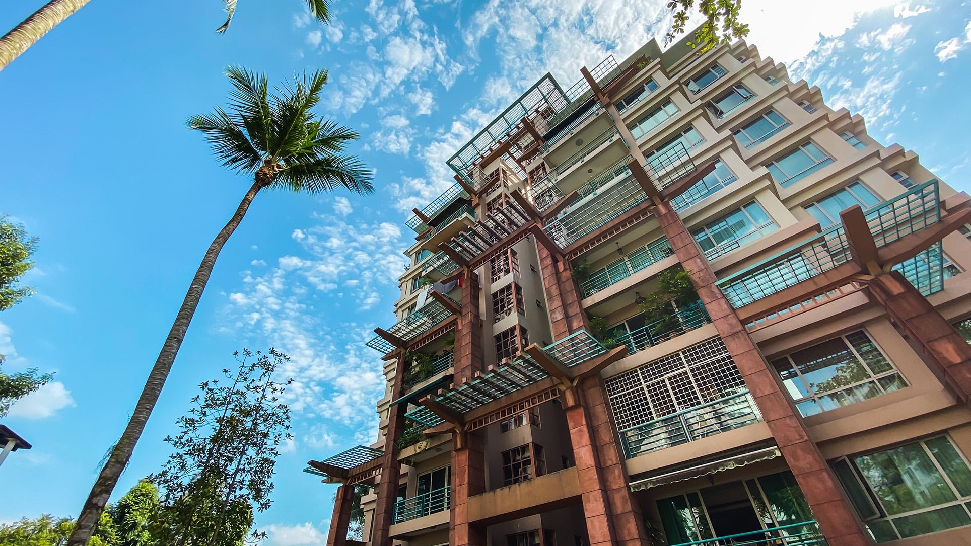 Maplewoods apartment blocks with glass balconies and metal pergolas under a blue sky with palm trees