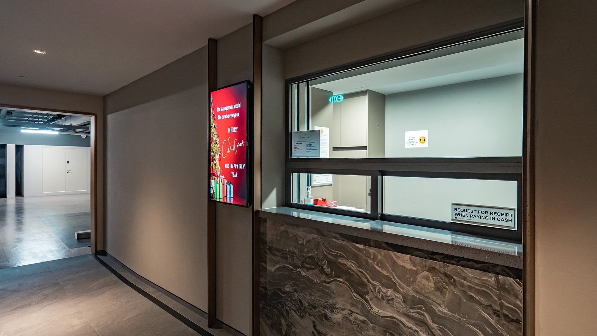 Security guard post with holiday message display screen next to a window counter in a building corridor