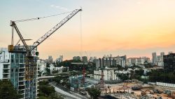 Tower crane beside a high-rise building at a construction site with housing blocks under a sunset sky