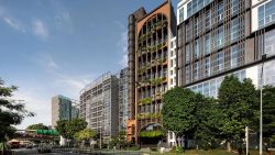 Street view of commercial buildings with vertical greenery cladding and modern glass facades under a blue sky