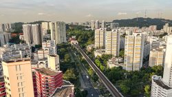HDB blocks with distinctive red and yellow highlights near a green park and MRT line in residential neighbourhood