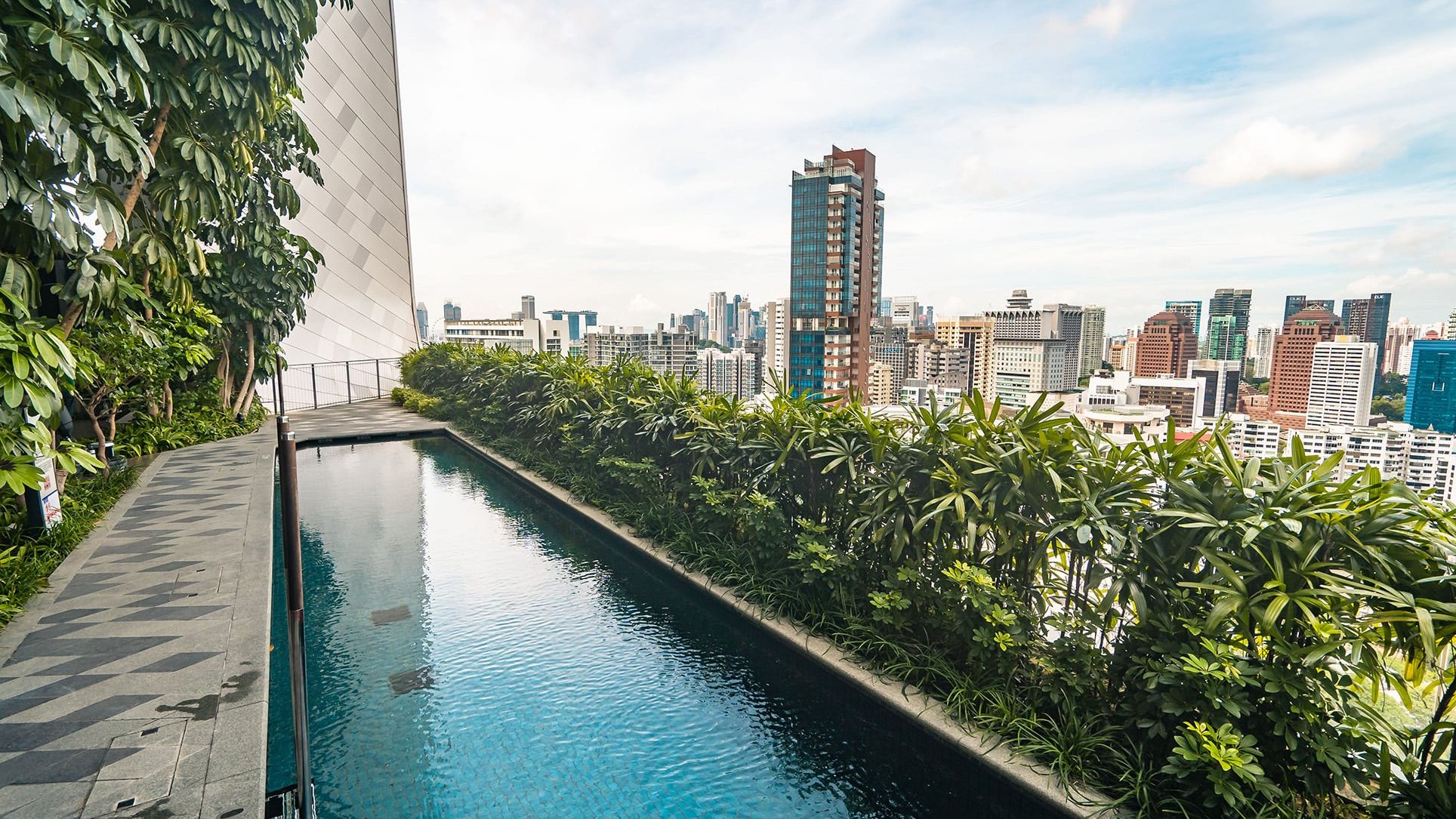 The Scotts Tower rooftop pool beside a walkway with greenery and city skyline in the background