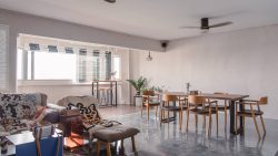 Living and dining area with wooden chairs, sofa with patterned throws, bar table by windows and ceiling fan