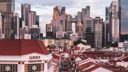 Chinatown shophouses with red tiled roofs and high-rise office buildings in background at dusk