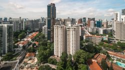 High-rise residential buildings and rows of low-rise houses with orange roofs amid green trees and city skyline