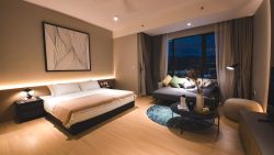 Bedroom with king-sized bed, bedside tables, a sofa with cushions, floor lamp, and large window with curtains at night