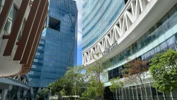 Modern office towers with glass facades and SYMBIOSIS signage surrounded by trees under blue sky