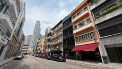 Shophouses and commercial buildings along a street with cars parked and city skyscrapers in the background