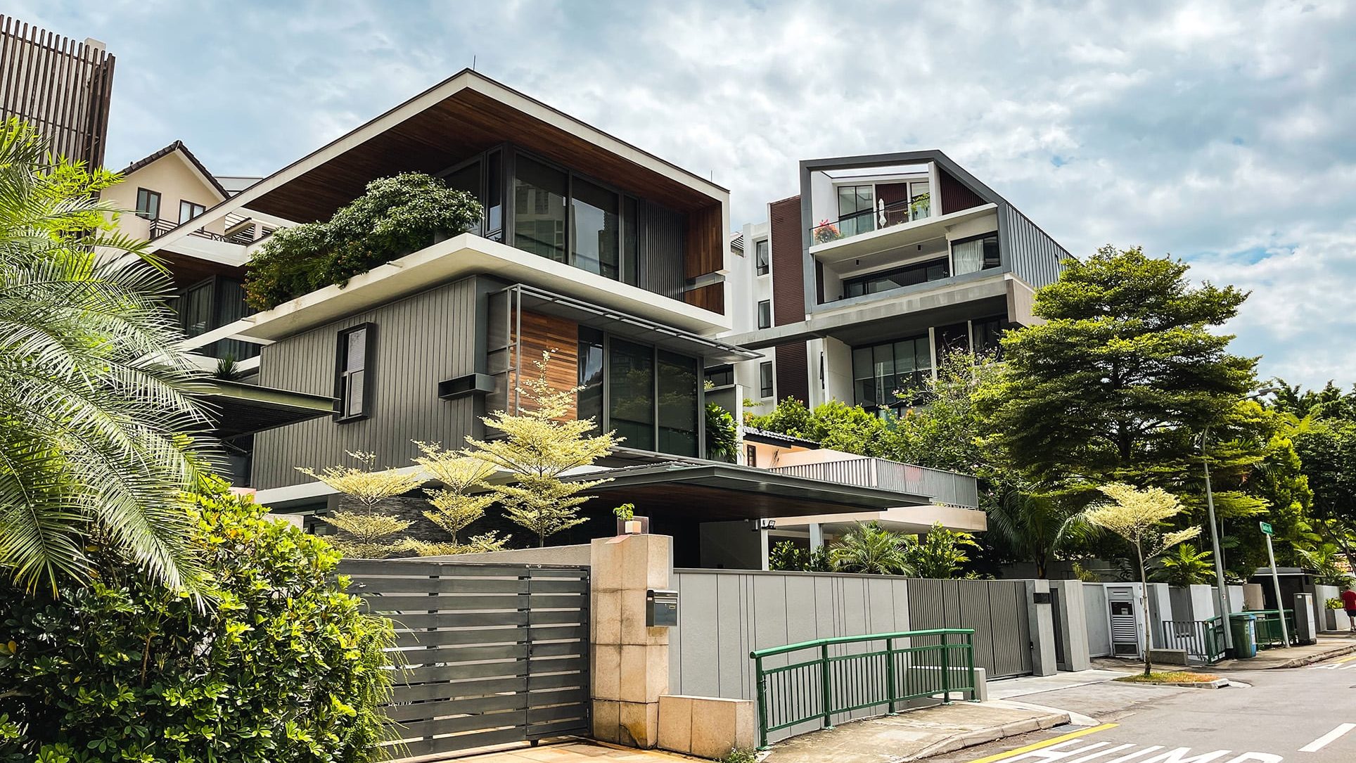 Modern multi-storey houses with large windows and greenery surrounding a quiet street corner
