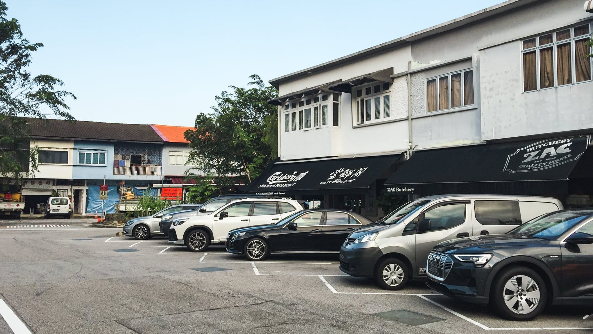 Two-storey shophouses including ZAC Butchery with cars parked in front on an asphalt street in daylight