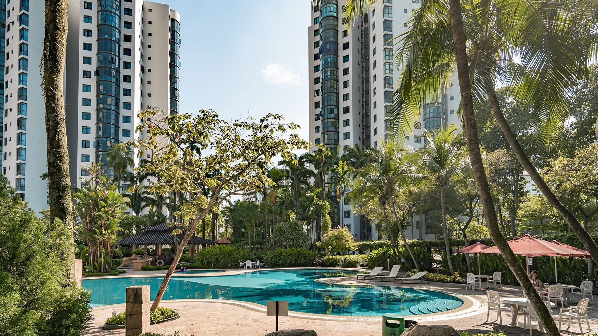 Parc Oasis apartment blocks behind a swimming pool and poolside seating surrounded by trees and greenery