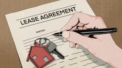 Hand holding pen signing lease agreement with house-shaped keychain and keys on paper