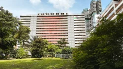 Pink and white public housing blocks behind trees and a grassy lawn under a partly cloudy sky