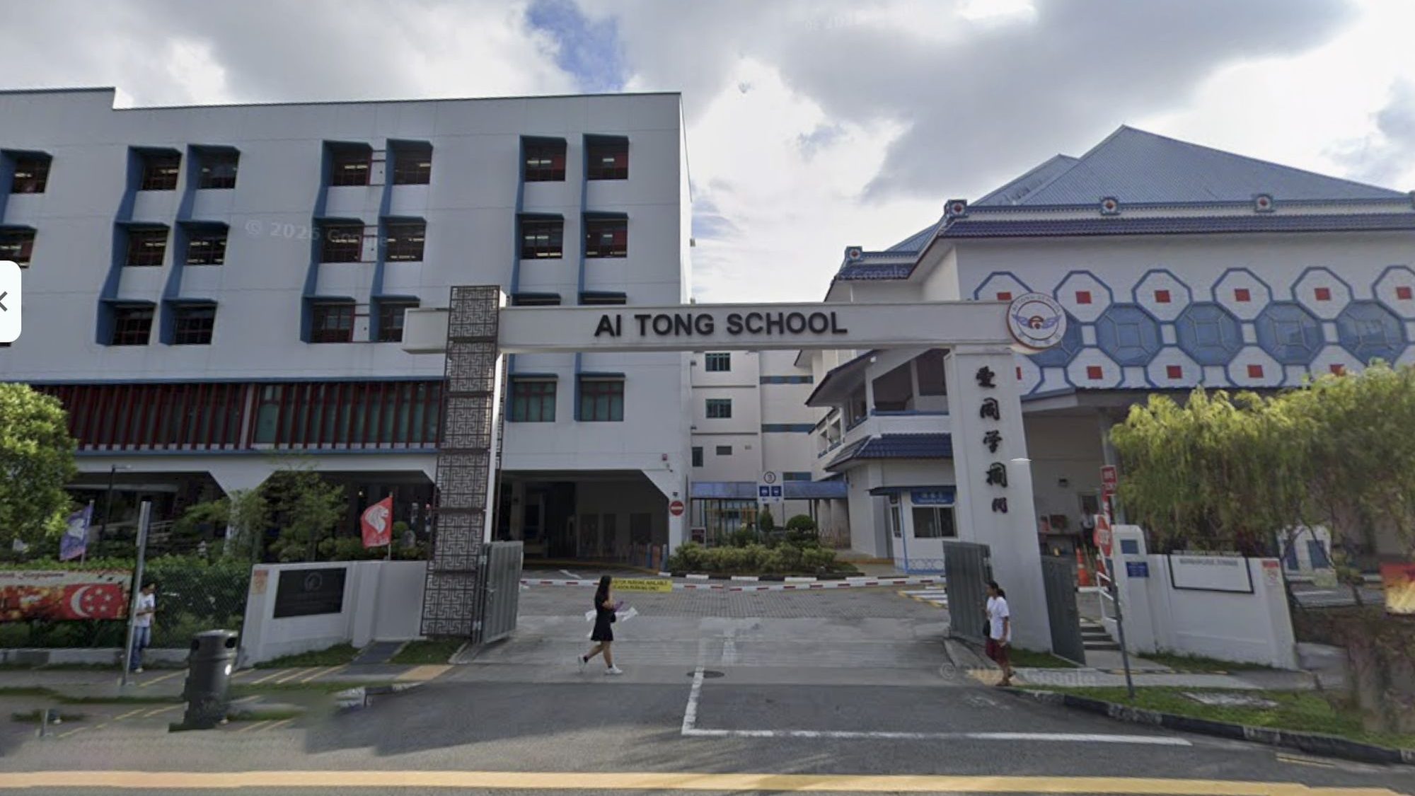Entrance gate and buildings of Ai Tong School with people walking nearby and cloudy sky above