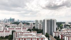 High-rise residential blocks and HDB flats under a cloudy sky with greenery and distant skyline