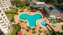 Bullion Park pool with surrounding sun loungers, palm trees, children’s playground, and tennis courts