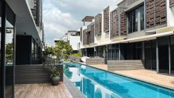 Modern residential blocks with a long swimming pool and wooden deck surrounded by plants under cloudy sky