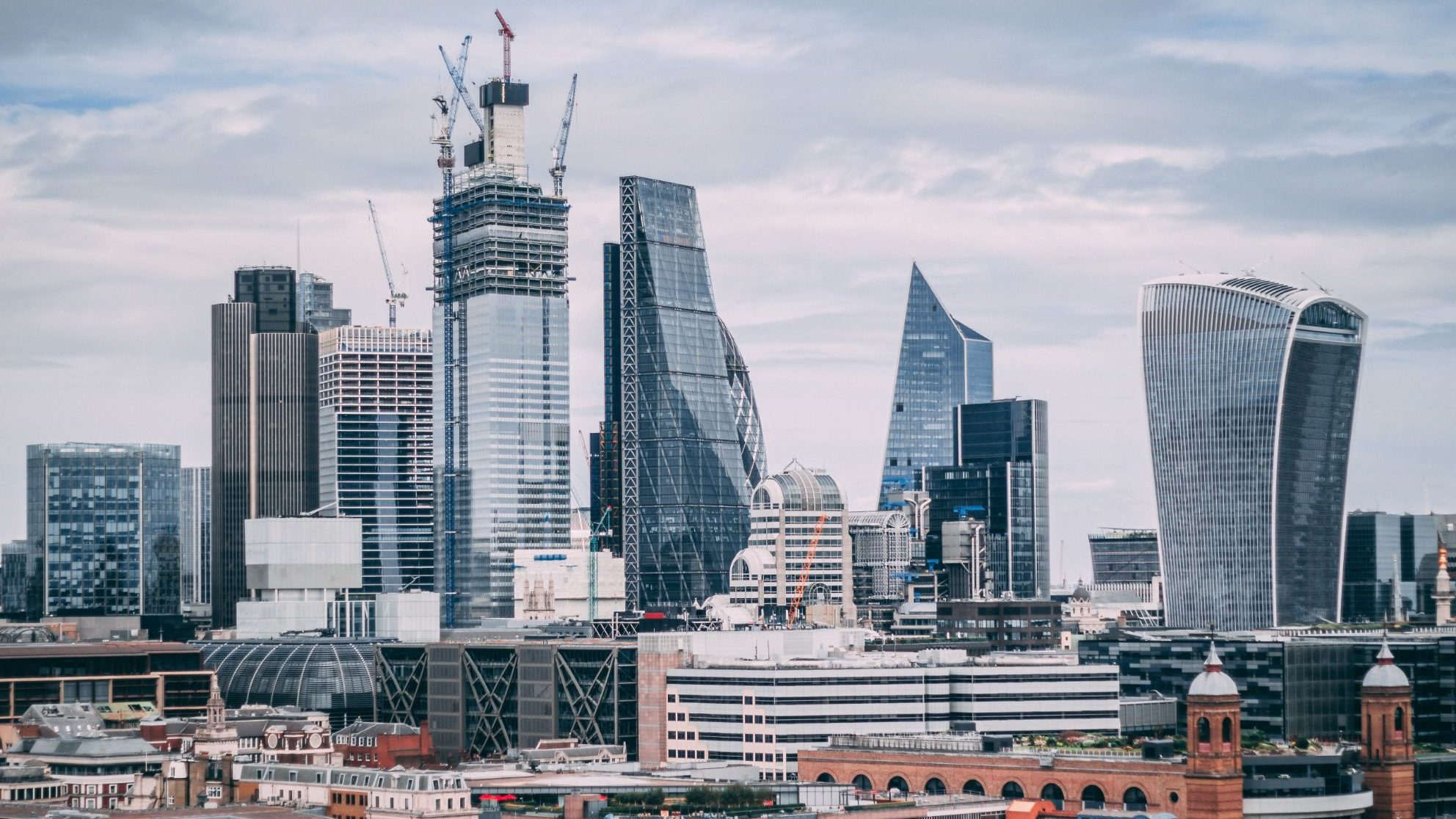Cluster of modern office skyscrapers with cranes amid partly cloudy sky in city centre