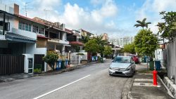 Two-storey terrace houses with tiled roofs along a street with parked cars and greenery