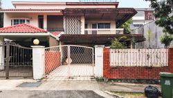 Detached house with red tiled roofs behind metal and wooden fences next to a green bin and black bag on pavement