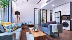 Living room with blue sofas, wooden coffee table, floor lamp, framed pictures, and kitchen appliances in cabinets