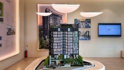 Architectural model of Hill House residential blocks displayed in a showroom with floor plans and digital screen