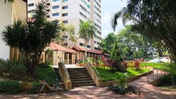 HDB block with red-tiled roof walkway, greenery, and parked bicycle near stairs and ramp pathway