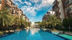 Parc Rosewood residential blocks flanking a large swimming pool with palm trees and pool chairs under a blue sky