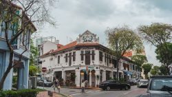 Two-storey conserved shophouse with black shutters and dragon motifs at street corner with pedestrians and vehicles