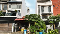 Two-storey terrace houses with balconies and greenery, featuring papaya trees and waste bins in front