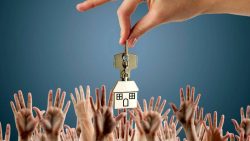 Hand holding a house-shaped keychain above many outstretched hands against a blue background