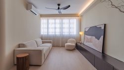 Living room with beige sofa, round cream chair, black wall-mounted cabinet, abstract artwork, and ceiling fan
