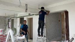 Two workers installing pipes and wiring in an unfinished residential interior under renovation